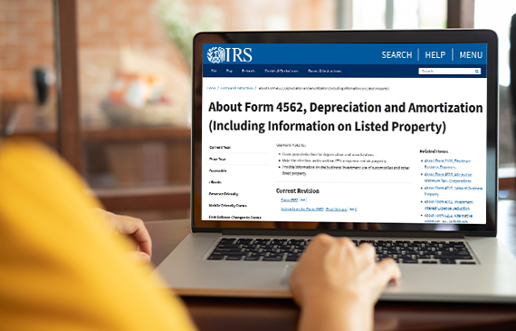 Over the shoulder view of a business owner using their laptop to visit the IRS's website to download Form 4562. Their screen says in bold black letters, Depreciation and Amortization.