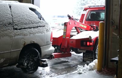 A red tow truck starts to tow a van covered in snow.